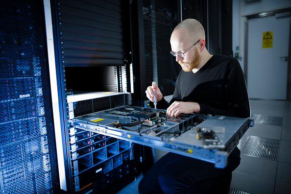 A technician using a screwdriver to repair a server pulled from a rack in a data center.