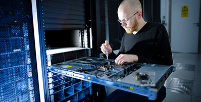 A technician uses a screwdriver to service a server pulled from a rack in a data center.