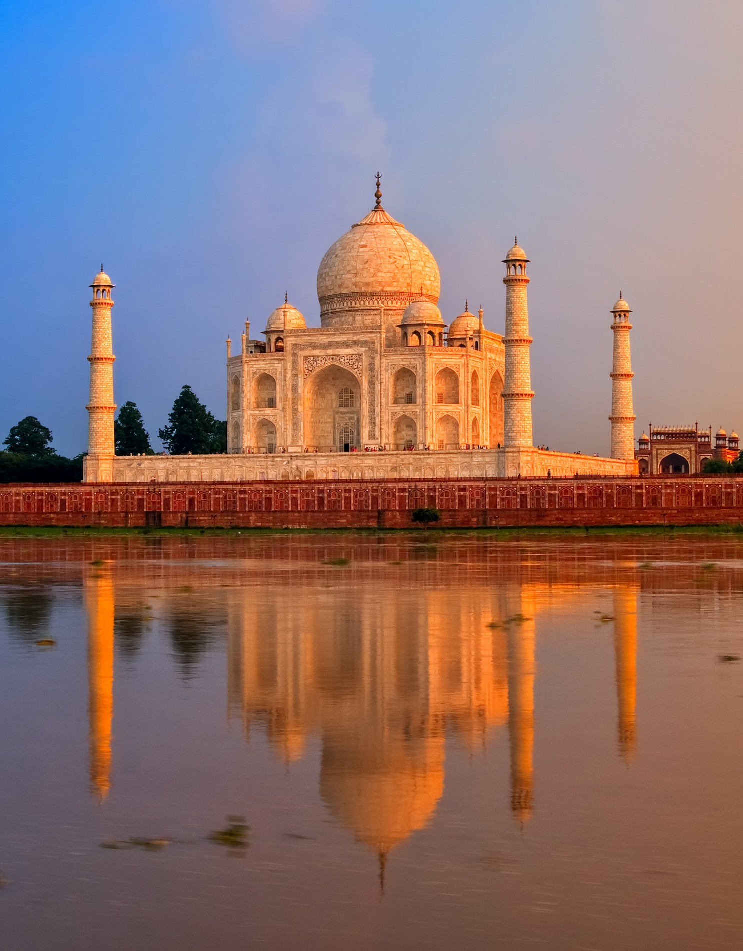 The Taj Mahal at sunset, reflected in the calm waters of the Yamuna River.