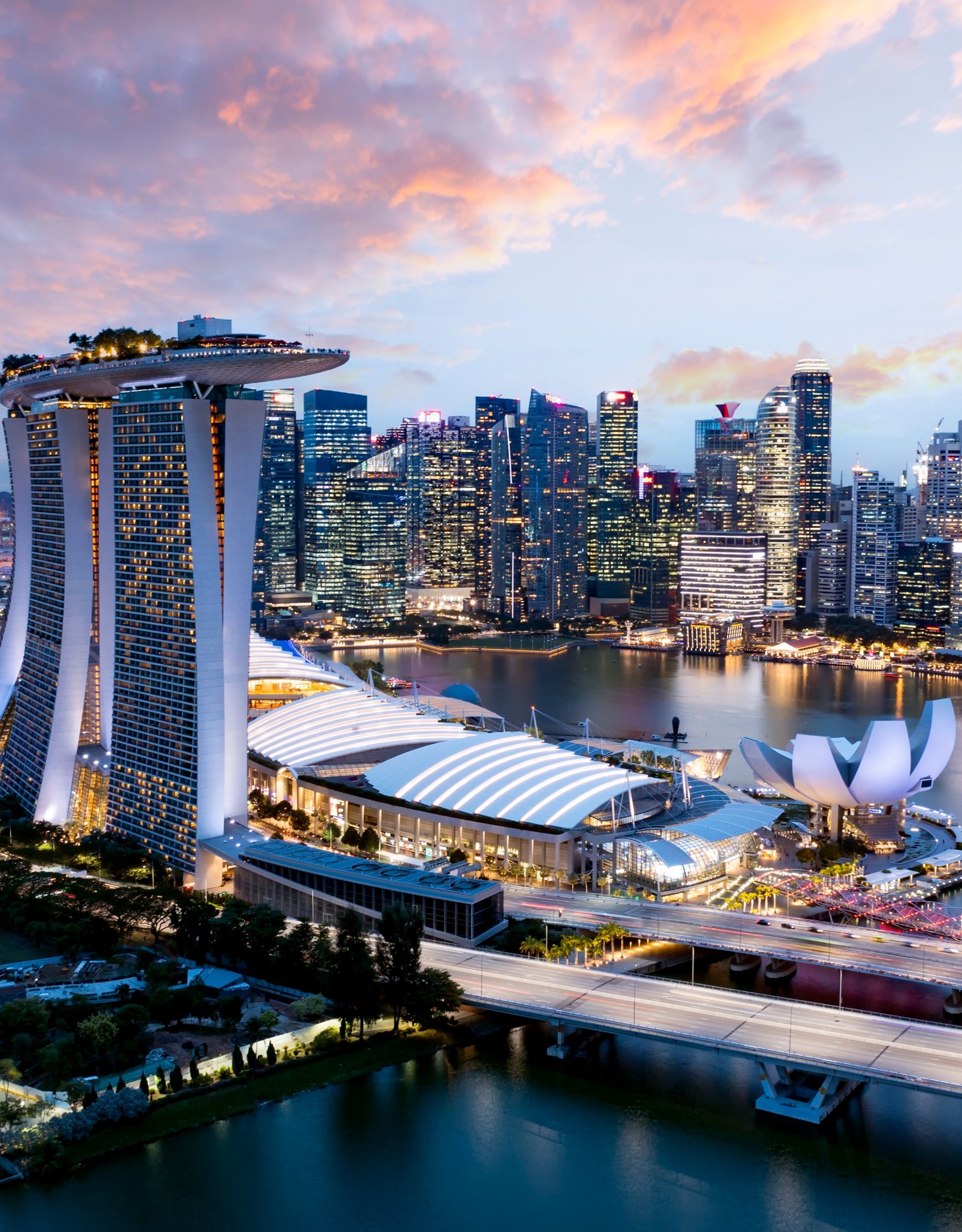 Aerial view of the Singapore skyline at sunset, featuring the Marina Bay Sands resort and the ArtScience Museum by the waterfront.