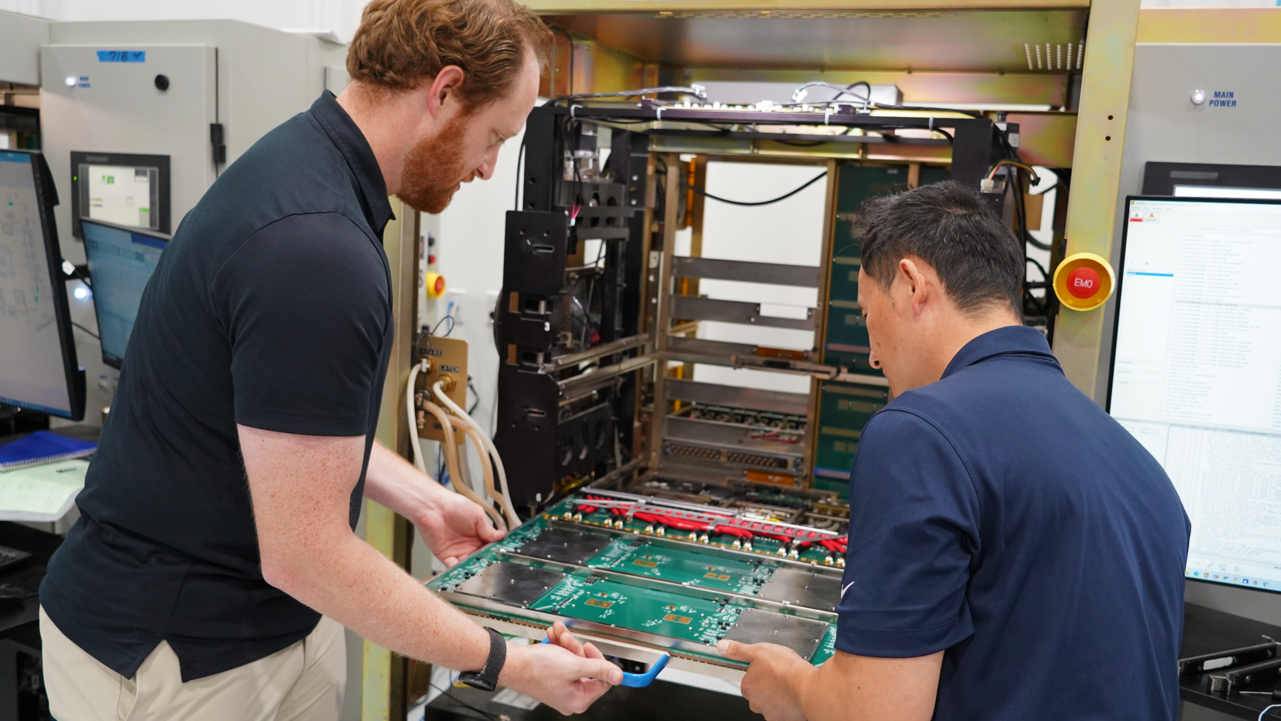 Two technicians inspect a large circuit board being installed into a server rack.